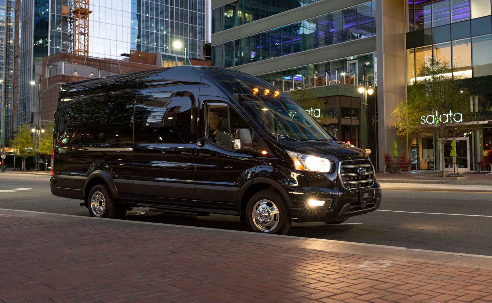 Black luxury shuttle van at night with the city skyline behind it